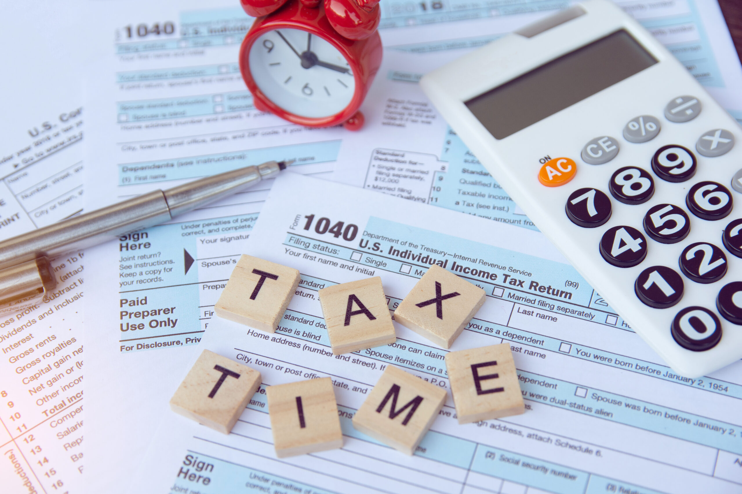 Tax Time Preparation in Shepparton Tax time with wooden alphabet blocks, red alarm clock, calculator and pen on 1040 tax form background